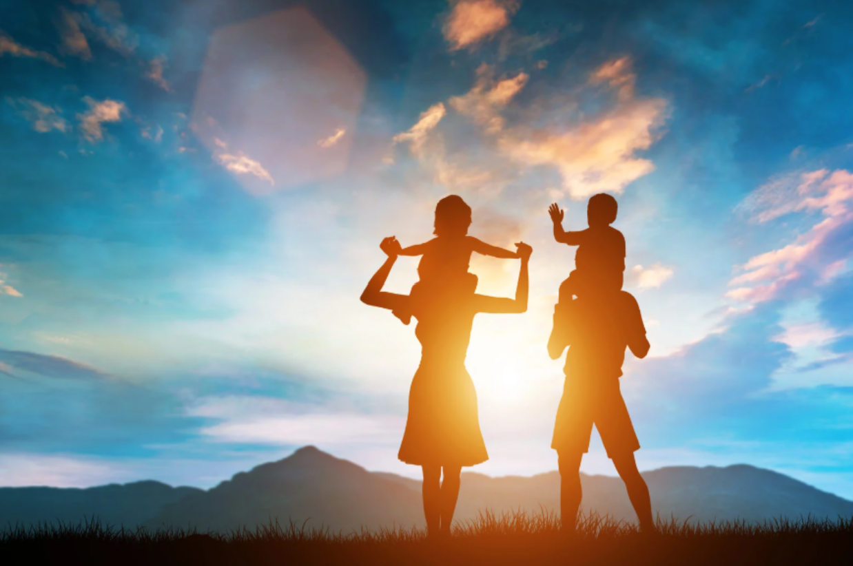 Parents walking with their kids on their shoulders in the sunset with mountains and a beautiful blue sky with clouds in the background.