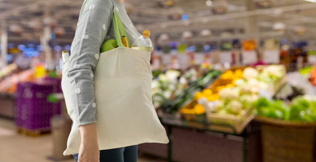 Sustainable Swaps. Eco-Friendly Swaps. Easy Sustainable Swaps. Easy Swaps. A woman walking in a grocery store with a reusable shopping bag.