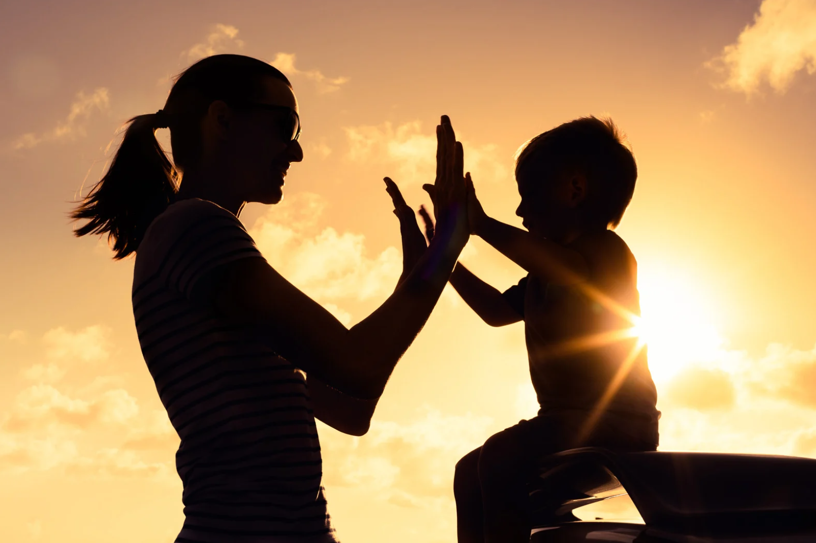 Mindful Parenting. Parenting Tips for Toddlers. Parenting Tips for Babies. Nurture Toddlers. Nurture Babies. Woman and son in shadow in front of a sunset high fiving.