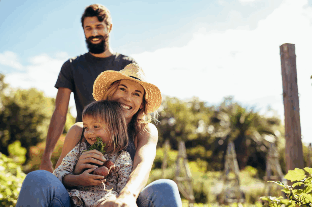 Mom and dad are outside in the garden, and their young daughter is holding fresh produce.