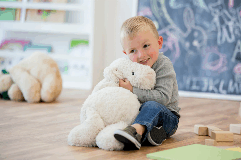 A boy on the floor hugging a stuffed animal.