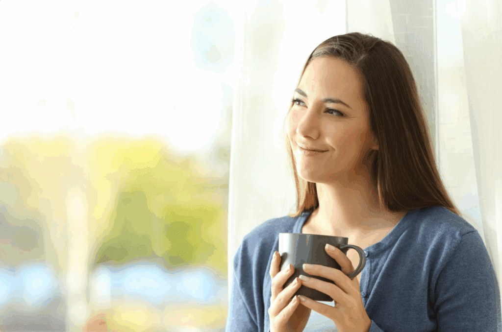 A young woman enjoying a mindful moment with a cup of tea or coffee by a window.